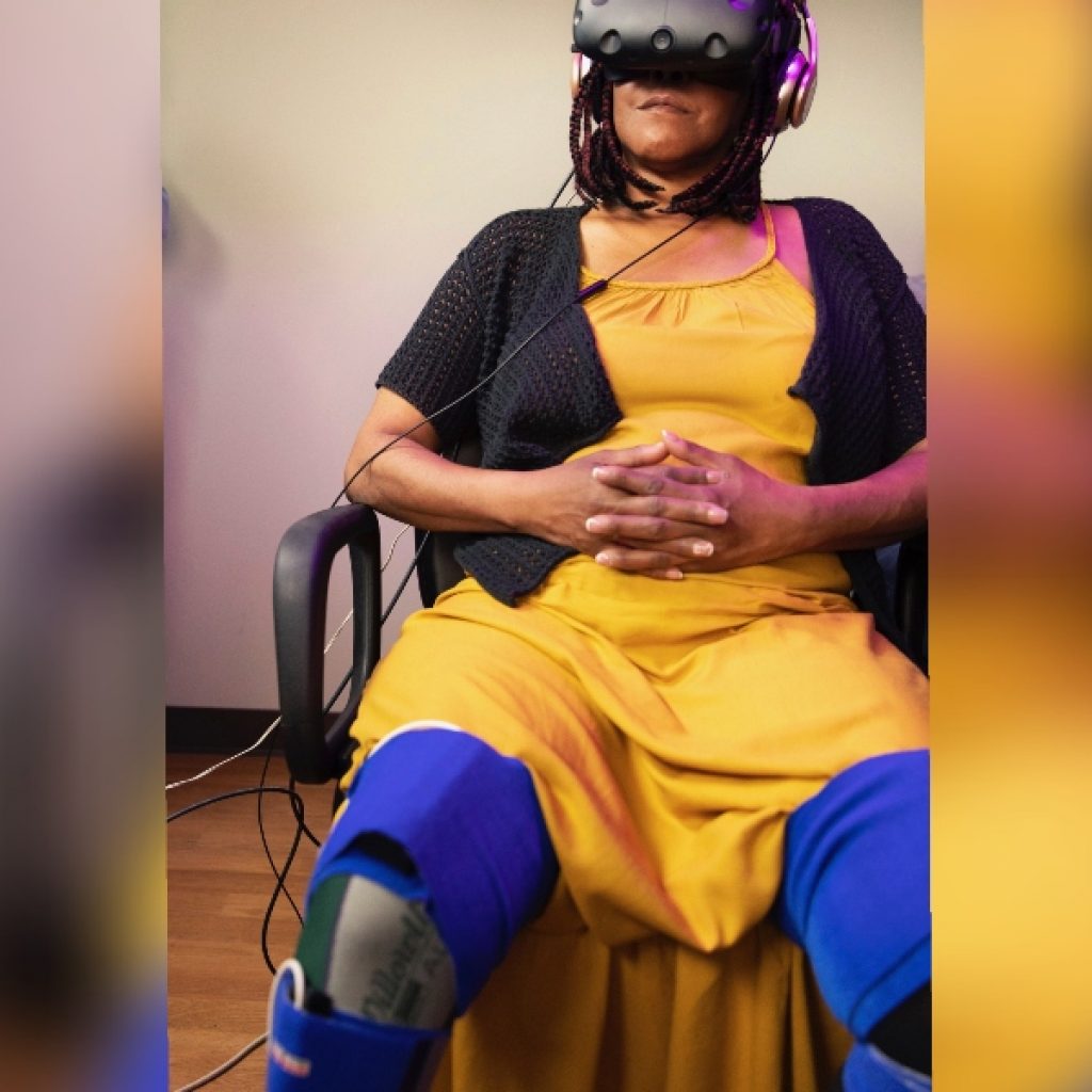 Woman with prosthetic leg sitting in chair while wearing a VR headset.